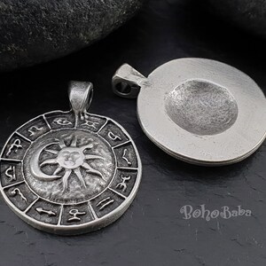 May include: Silver pendant with a sun and moon design surrounded by zodiac symbols. The pendant is on a dark gray background.