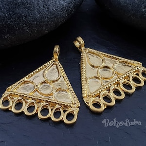 May include: Two gold-tone triangle-shaped metal pendants with intricate designs and a row of open circles at the bottom. The pendants are on a dark grey background.