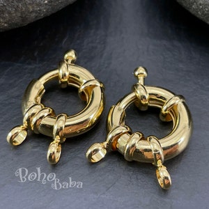 Puede incluir: Dos cierres de anillo de metal dorado con un diseño trenzado. Cada cierre tiene tres pequeños bucles para sujetar a un collar o pulsera.