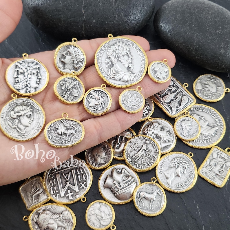 Puede incluir: Una colecci&oacute;n de colgantes con forma de moneda de color plateado con bordes dorados. Los colgantes presentan varios dise&ntilde;os cl&aacute;sicos, incluyendo perfiles de figuras, animales y patrones intrincados. Los colgantes son de diferentes tama&ntilde;os y formas, con un lazo en la parte superior para colgar.