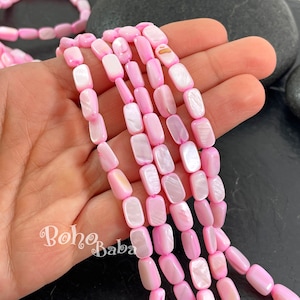 Può includere: Una collana di perline rettangolari in conchiglia rosa e bianca. Le perline sono lisce e hanno una lucentezza iridescente naturale.
