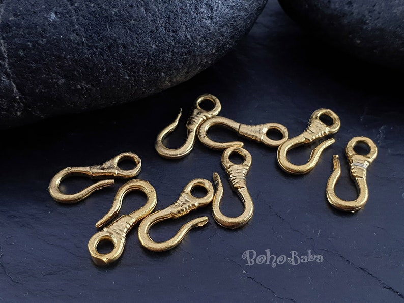 May include: A close-up of eight gold-toned metal lobster clasps. The clasps are scattered on a black surface.