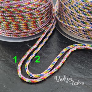May include: Two spools of colorful embroidery floss, one pink with red, yellow, green, and blue threads, and one pink with blue, yellow, red, and green threads. The spools are labeled 1 and 2.
