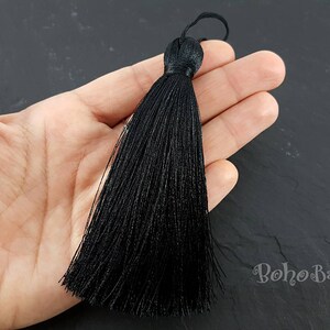 K&ouml;nnte beinhalten: Eine lange, schwarze Quaste mit einer Schlaufe oben. Die Quaste besteht aus vielen Str&auml;ngen schwarzen Fadens, die oben zusammengebunden sind. Die Quaste wird in einer Hand vor einem dunklen Hintergrund gehalten.