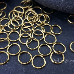 Peut inclure: Un tas de anneaux de jonction dor&eacute;s, un type de composant de bijoux, sur une surface gris fonc&eacute;. Les anneaux sont petits et ronds, et ils sont parfaits pour la fabrication de bijoux.