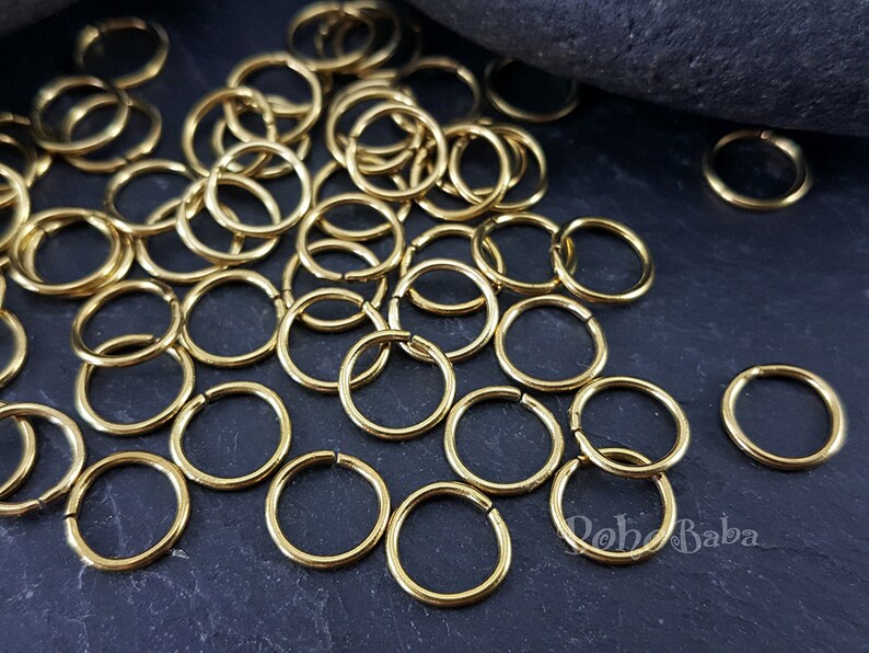 Peut inclure: Un tas de anneaux de jonction dor&eacute;s, un type de composant de bijoux, sur une surface gris fonc&eacute;. Les anneaux sont petits et ronds, et ils sont parfaits pour la fabrication de bijoux.