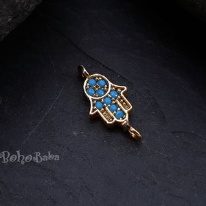 Puede incluir: Encanto de mano de hamsa en tono dorado con detalles de esmalte azul. El encanto tiene un bucle en la parte superior para sujetarlo a un collar o pulsera.