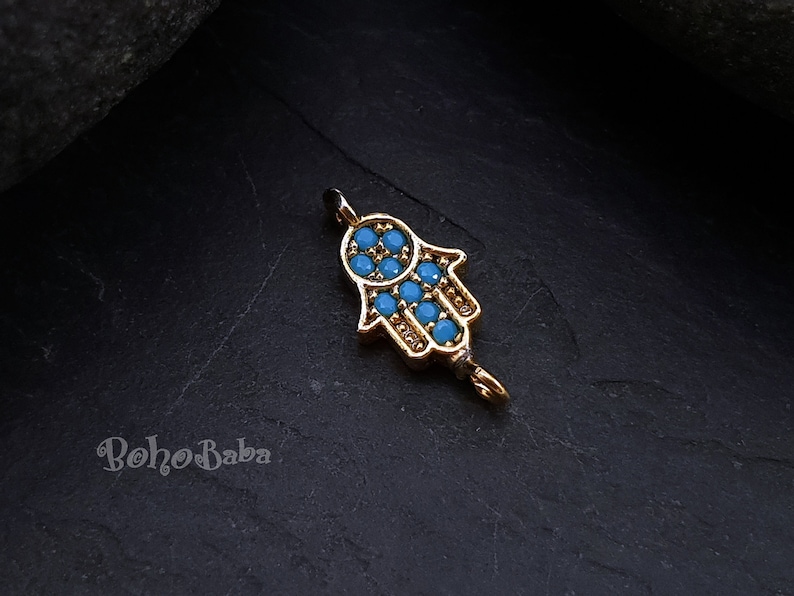 Puede incluir: Encanto de mano de hamsa en tono dorado con detalles de esmalte azul. El encanto tiene un bucle en la parte superior para sujetarlo a un collar o pulsera.