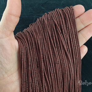 May include: A strand of dark brown seed beads, approximately 2mm in diameter, arranged in rows on a hand. The beads are uniform in size and shape, and have a slightly matte finish.