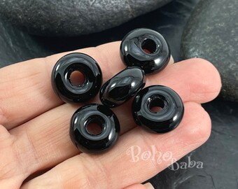 May include: Five black donut-shaped beads with a hole in the center. The beads are glossy and have a smooth surface.