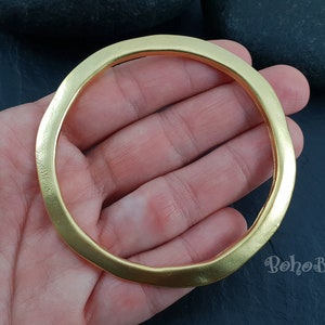 May include: A thick, gold-coloured metal bangle bracelet. The bracelet is smooth and has a slightly rounded shape.