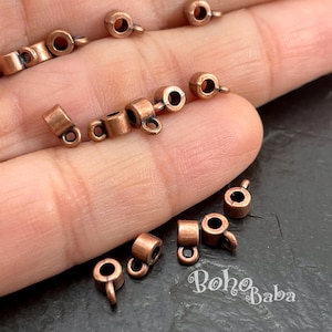 May include: A collection of small, copper-coloured metal jewellery findings, each featuring a cylindrical body with a single attached loop. These components are designed for jewellery making and are shown in a metallic finish with a warm, reddish-brown tone.