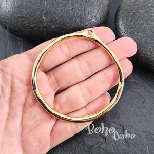 May include: Gold-toned metal ring with a smooth, rounded surface. The ring has a small hole at the top for attaching a charm or pendant.