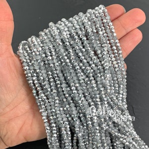 May include: A strand of silver faceted glass beads. The beads are small and round, with a shiny, metallic finish.