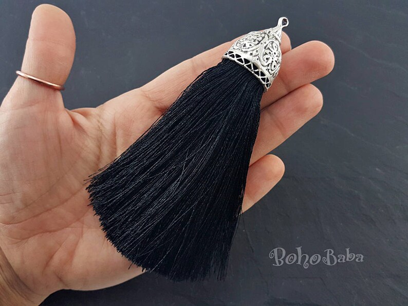 Puede incluir: Borla negra con una parte superior de metal plateado. La borla est&aacute; hecha de finos hilos de tela y tiene una parte superior de metal decorativa y adornada.
