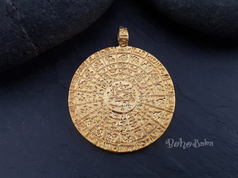 May include: Gold-toned pendant featuring a circular design with intricate details and raised lettering. The pendant is approximately 2 inches in diameter.
