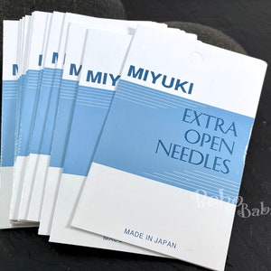 May include: A stack of white and blue packaging cards for Miyuki Extra Open Needles. The cards are made in Japan.