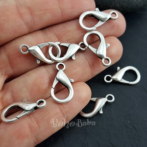 May include: A close-up of silver-toned lobster clasps, a type of fastener used in jewelry making.