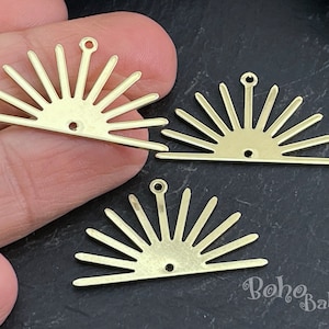 以下が含まれることがあります： 上部と下部に穴が開いた、ゴールドメタル製のサンバーストチャームが3つ。チャームの幅は約5cm、高さは約2.5cmです。