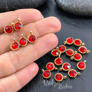 May include: A close-up of red rhinestone charms with gold-toned settings. The charms have a loop at the top for attaching to jewelry or other crafts.