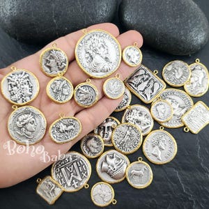 Puede incluir: Una colecci&oacute;n de colgantes con forma de moneda plateada con bordes dorados. Los colgantes presentan varios dise&ntilde;os de relieve cl&aacute;sicos, incluyendo retratos y figuras mitol&oacute;gicas. Algunos colgantes son redondos, otros rectangulares u ovalados.