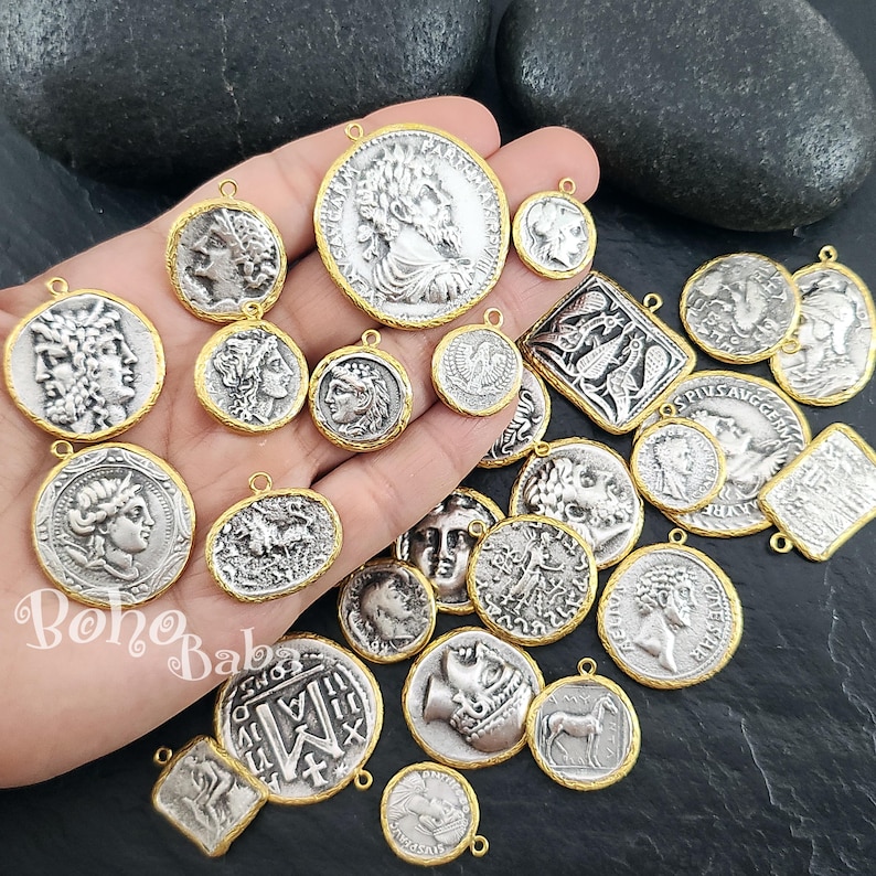 Puede incluir: Una colecci&oacute;n de colgantes con forma de moneda plateada con bordes dorados. Los colgantes presentan varios dise&ntilde;os de relieve cl&aacute;sicos, incluyendo retratos y figuras mitol&oacute;gicas. Algunos colgantes son redondos, otros rectangulares u ovalados.