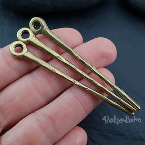 Puede incluir: Tres horquillas de metal dorado con extremos redondeados. Las horquillas están dispuestas en forma de abanico y tienen una textura martillada.