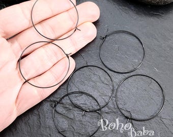 May include: Five black hoop earrings, each with a simple circular design. The earrings are displayed on a hand and a dark gray surface.