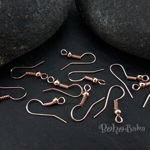 May include: A close-up of rose gold earring hooks. The hooks are made of metal and have a spring-loaded closure. The hooks are arranged on a black surface.