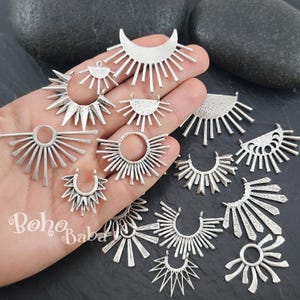 Könnte beinhalten: Eine Sammlung von silberfarbenen Sonnenstrahl-Anhängern und -Anhängern in verschiedenen Designs. Die Anhänger weisen strahlenförmige Linien und Halbmondformen auf, ideal für die Schmuckherstellung. Der Text "Boho Baba" ist enthalten.