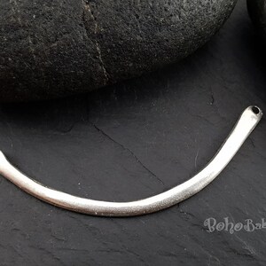 May include: Silver metal connector with two holes, shaped like a curved line. The connector is on a dark gray surface.