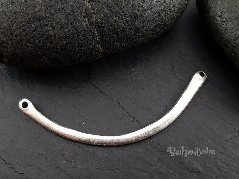 May include: Silver metal connector with two holes, shaped like a curved line. The connector is on a dark gray surface.