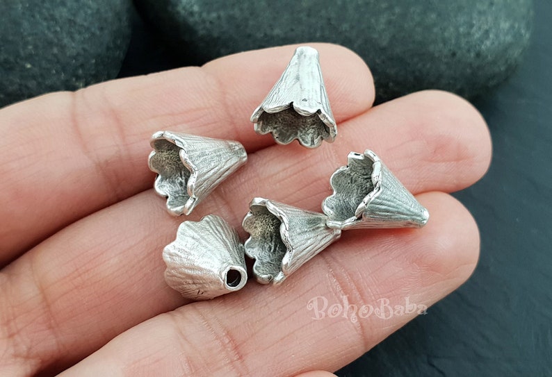 May include: Five silver metal cone-shaped bead caps with scalloped edges. The caps are approximately 1 inch in diameter.