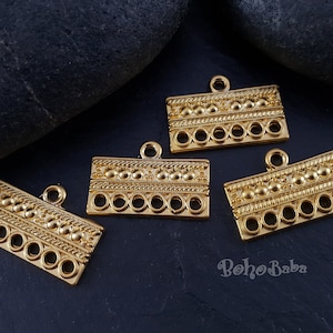 May include: Four gold-toned metal connector pieces with a decorative beaded design and five holes each. The pieces are on a black background.