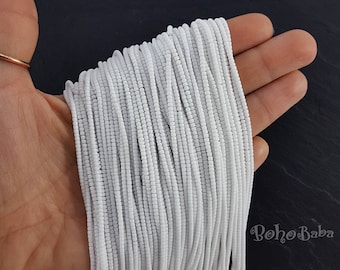 May include: A close-up of a bundle of white seed beads. The beads are small and round, and they are arranged in a neat, even row. The beads are perfect for making jewelry or other crafts.