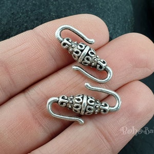May include: Two silver-toned metal clasps with intricate designs. The clasps are open and ready to be attached to a necklace or bracelet.