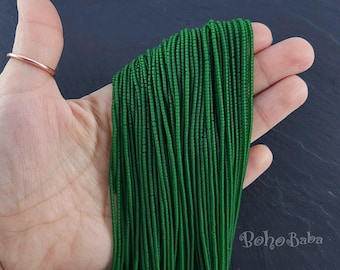 May include: A close-up of a hand holding a bundle of green seed beads. The beads are arranged in rows and are approximately 1.5 mm in diameter.
