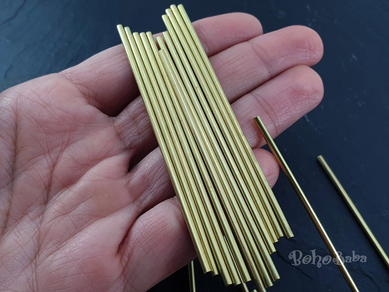 May include: A close-up of a hand holding a bundle of 16 gold-colored metal rods. The rods are approximately 6 inches long and have a smooth, polished finish.