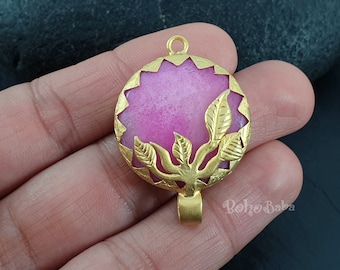 Peut inclure: Pendentif en or avec une pierre rose et un motif découpé de feuilles. Le pendentif est rond et possède une boucle en haut pour attacher une chaîne.
