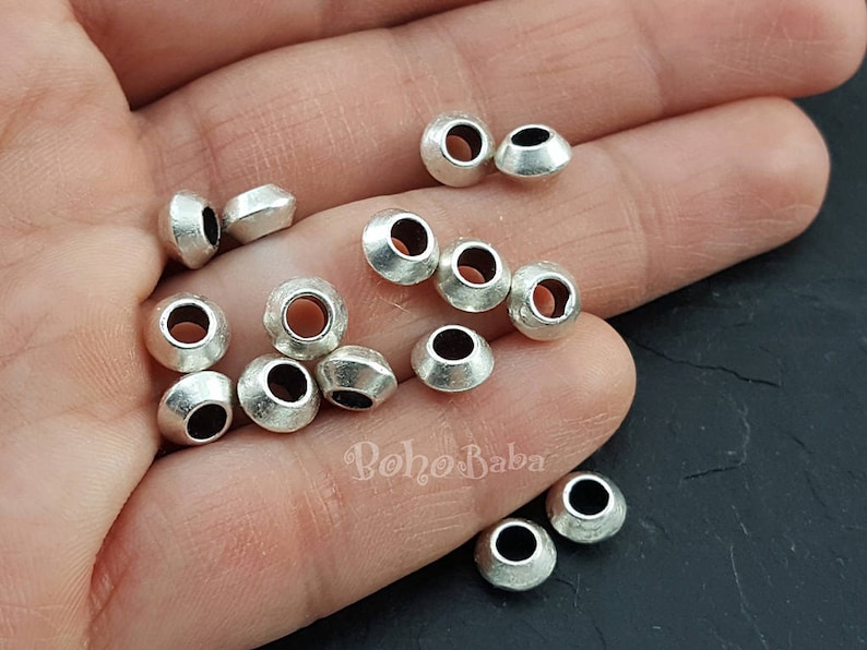 May include: A close-up of a pile of silver metal beads. The beads are round and have a slightly domed shape. They are perfect for jewelry making or other craft projects.
