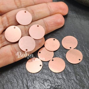 Puede incluir: Colección de abalorios redondos de metal color cobre con un pequeño agujero en la parte superior para ensartar. Los abalorios tienen un acabado cepillado y se muestran en una mano. Ideal para la fabricación de joyas.