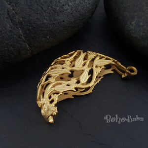 May include: Gold-toned metal pendant with a delicate, intricate design resembling a stylized floral pattern. The pendant has a loop at the top for attaching to a chain or cord.