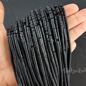 May include: A strand of black round beads, each bead is approximately 1.2 cm long and has a slightly textured surface. The beads are strung on a clear thread and are arranged in a straight line.
