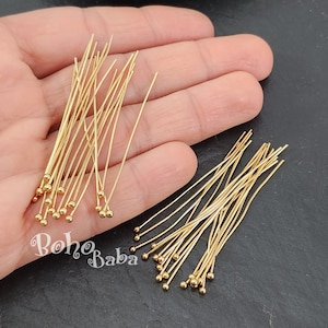 Puede incluir: Primer plano de dos paquetes de alfileres de cabeza redonda de color dorado. Los alfileres están dispuestos en un patrón aleatorio y miden aproximadamente 2,5 cm de largo.