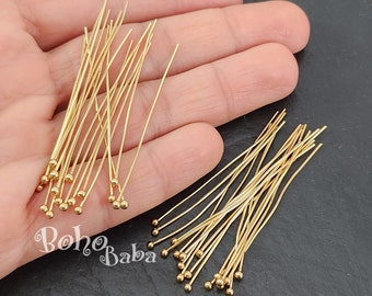 May include: A close-up of two bundles of gold-colored head pins with round heads. The pins are arranged in a random pattern and are approximately 1 inch in length.