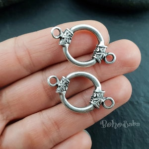 Puede incluir: Dos cierres de metal plateados con diseños florales ornamentados. Cada cierre tiene un anillo circular y un bucle más pequeño para sujetarlo a un collar o pulsera.