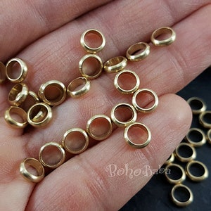 May include: A close-up of a hand holding a large quantity of small, gold-colored metal rings. The rings are smooth and round, and they appear to be made of brass.