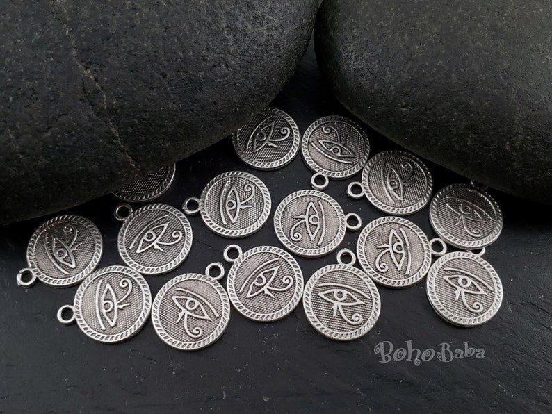 May include: Silver charm pendants with the Eye of Horus symbol. The charms are round and have a textured edge. They are perfect for jewelry making or crafting.