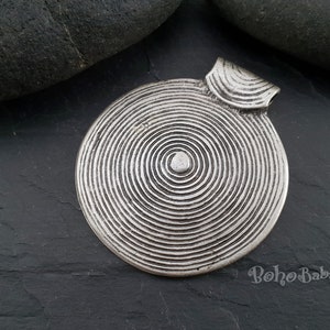 May include: Silver pendant with a circular design featuring concentric circles. The pendant has a loop at the top for attaching to a chain.