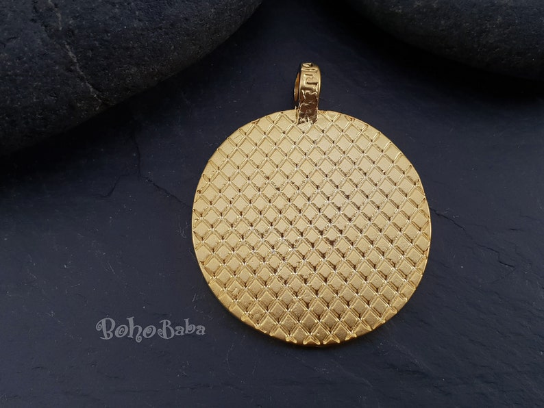 May include: Gold-toned round pendant with a textured diamond pattern. The pendant has a loop at the top for attaching to a chain.